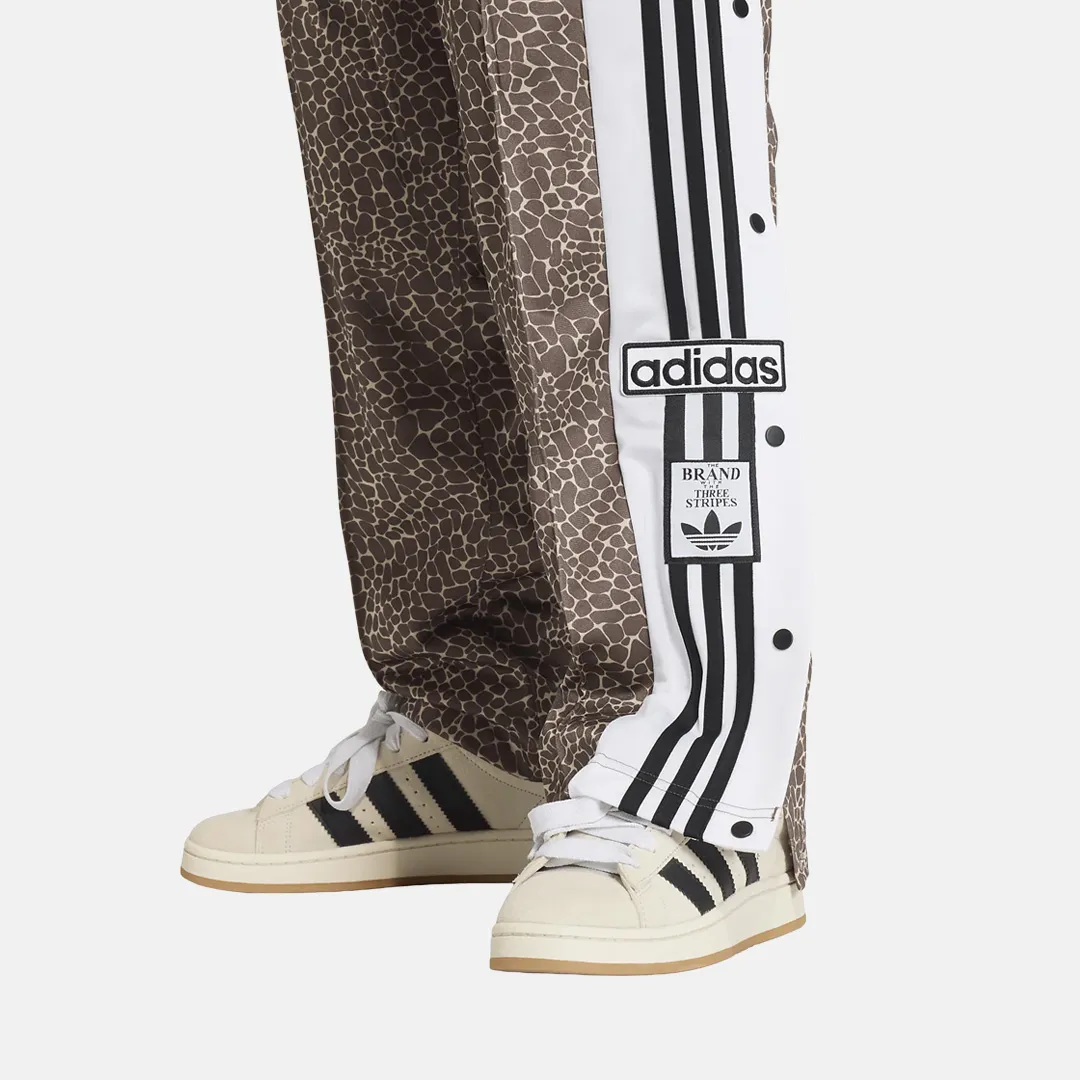 Brunmönstrade byxor med vit sidopanel med Adidas-logotyp, tre svarta ränder och vita sneakers med svarta ränder.